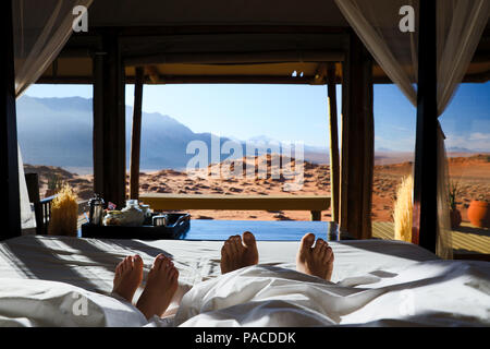 Paar im Bett Faulenzen auf Hochzeitsreise mit Vista Ansicht der Namib auf wolwedans Lodge Stockfoto