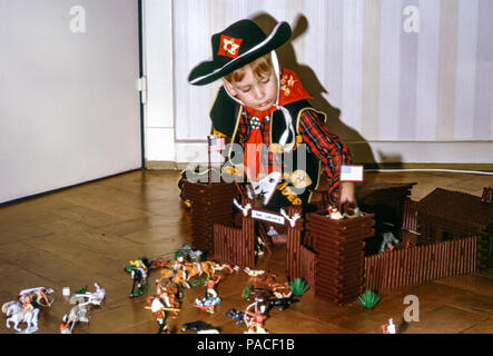 Boy trägt einen Cowboy Hut spielt mit einem Kunststoff-Amerikaner Toy Fort genannt Fort Laramis mit Spielzeug Cowboys und Indianer Auf einem Parkettboden in den 1960er Jahren Stockfoto