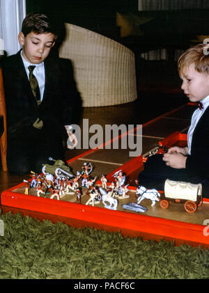 Zwei Jungen, Brüder, trugen Sonntagskleidung mit Anzügen und Krawatten und spielten Cowboys und Indianer in einem Familiensitzraum in den 1960er Jahren Stockfoto