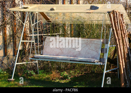 Alte hausgemachte Hollywoodschaukel Hollywood Schaukel auf einer Wiese, die von Pflanzen in den Garten mit einem Zaun und Bäumen umgeben. Stockfoto