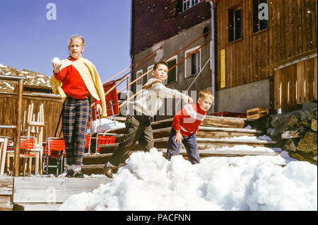 Drei Kinder, ein Mädchen und zwei Jungen, Schwester und Brüder, die in den 1960er Jahren Schneebälle in einem Skigebiet in den Alpen, Österreich, warfen Stockfoto