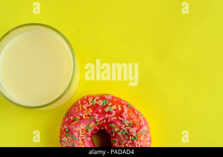 Das Glas Milch und Donuts auf Pastell gelben Hintergrund. Süße Krapfen. Flatlay. Copyspace rechts Stockfoto
