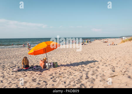 Der Mann und die Frau sitzt auf einer Decke unter einem orange Sonnenschirm am Strand am Nachmittag Sonnenschein, Rorvig, Dänemark, 16. Juli 2018 Stockfoto