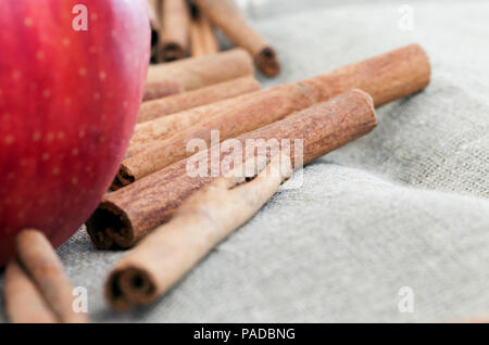 Liegend auf der Tischdecke aus Leinen gesamte Sticks von duftenden Zimt, auf der einen Seite ist eine reife rote Apfel, Zimt ist mit einem Apple eine Torte zu machen verwendet Stockfoto