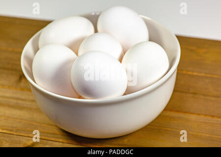 Eine Gruppe von Eiern in einer tiefen weiße Schüssel neben einem schneebesen Warten auf der Küchenchef Ihnen in einer Mahlzeit zu verwenden Stockfoto