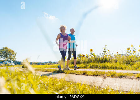 Zwei gesunde ältere Leute joggen auf einer Landstraße im Sommer Stockfoto