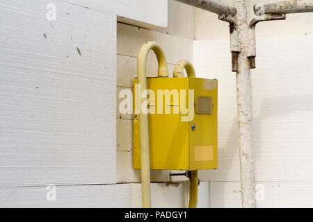 Close-up gelb Gas meter Box mit Verbindungsleitungen hängen an der Ecke des Hauses Wand mit weißen Polyurethan-hartschaum styrophome Blätter isoliert. Stockfoto