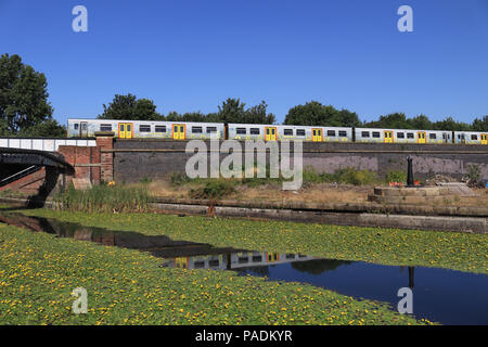 A Mersey rail train travelling from Liverpool to Southport crosses the Leeds and Liverpool canal near the Caroline Street footbridge in Bootle. Stockfoto