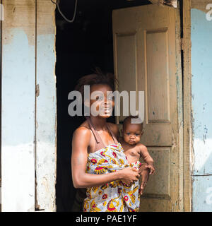 LIBREVILLE, Gabun - Mar 6, 2013: Unbekannter gabunischen Frau hält Ihr Baby und bleibt auf der Veranda in Gabun, Mar 6, 2013. Menschen in Gabun Leiden von Po Stockfoto