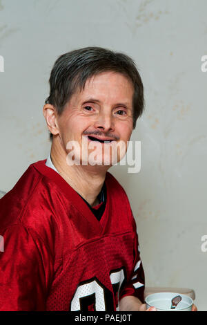 Portrait eines älteren Mann mit Down-syndrom. Er hält eine Schale mit einem Löffel in der IT und ein Lächeln für die Kamera. Er hat nicht mehr die Zähne. Stockfoto
