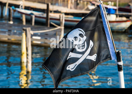 Eine Piratenflagge in einem Hafen mit Booten auf dem Hintergrund Stockfoto