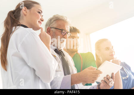 Eine Gruppe von Ärzten sind mit einem digitalen Tablet für die Diskussion über Diagnose und lächelnd beim Stehen vor seinem Patienten. Stockfoto