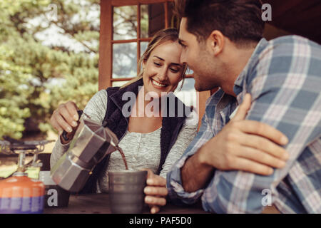 Glückliche junge Frau Kaffee zu ihrem Freund. Paar Kaffee am Morgen. Frau gießen Kaffee in die Tasse von ihrem Freund. Stockfoto