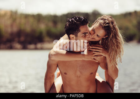 Portrait der romantischen jungen Mann huckepack seine Freundin. Junges Paar, das Spaß am Seeufer. Stockfoto