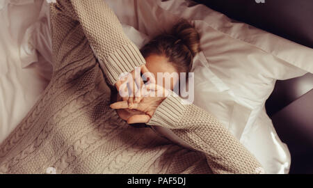 Blick von oben auf die liegende Frau auf dem Bett mit den Händen über Gesicht. Weibliche ruht auf dem Bett mit den Händen über ihr Gesicht. Stockfoto