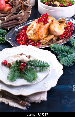 Gebackenes Huhn auf einer Servierplatte mit roten Beeren. Auf einem blauen Holztisch mit einer Schüssel, mit Platten Stockfoto