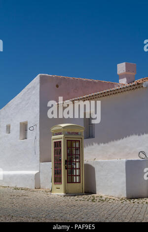 Platz mit Kopfsteinpflaster gefliest. Weiße Fassade des traditionellen Häusern. Beige Farbe der retro styled Telefonzelle. Strahlend blauen Himmel. Cacela Velha Stockfoto