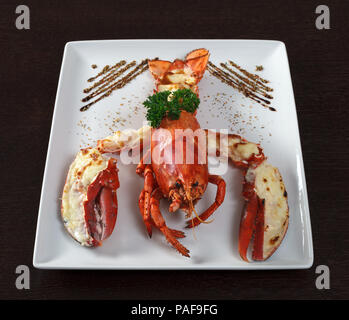 Hummer. Ein Gericht mit Hummer und Petersilie. Weiße Platte auf hölzernen Tisch. Von der Seite. Stockfoto