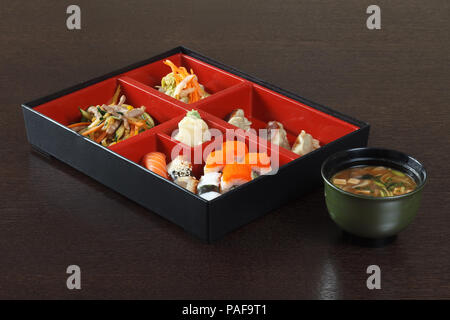 Bento Box mit Sushi und Brötchen, Miso Suppe auf einem Holztisch. Stockfoto