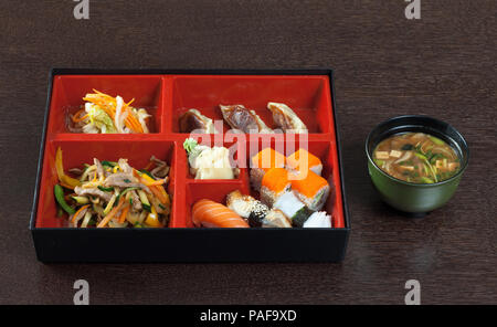 Bento Box mit Sushi und Brötchen, Miso Suppe auf einem Holztisch. Stockfoto