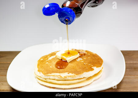 Gießen Sirup aus einem blauen Spitze Flasche auf den Platz von Butter auf einem Stapel goldene Pfannkuchen warten gegessen zu werden. Stockfoto