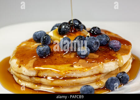 Gießen Sirup über die Butter auf die blaubeere Stapel Pfannkuchen auf dem Küchentisch warten gegessen zu werden. Stockfoto