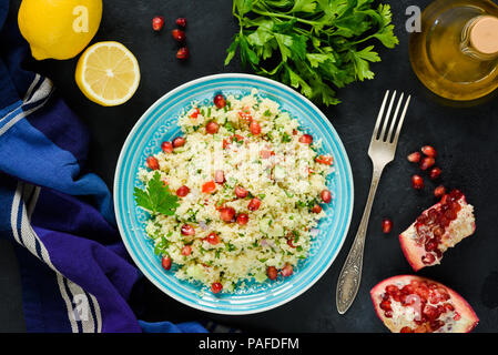 Tabbouleh Salat mit Couscous und auf blauen Platte Granatapfel auf dunklen konkreten Hintergrund. Ansicht von oben arabisches Essen Stockfoto