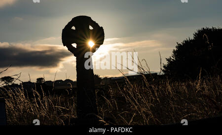 Silhouette einer Cornish Granit Keltisches Kreuz mit der untergehenden Sonne Sternenexplosion durch die Mitte des Kreuzes Stockfoto