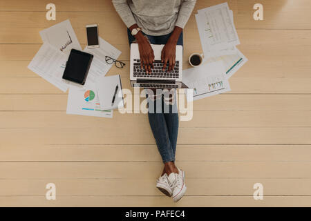 Blick von oben auf eine Frau Unternehmer auf dem Laptop zu Hause sitzen. Frau sitzt auf dem Boden arbeiten zu Hause auf dem Laptop Computer mit Kaffee und Business Stockfoto