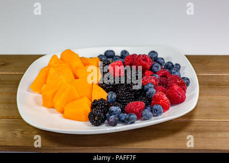 Eine Platte der cantaloup, Heidelbeeren, Himbeeren, Brombeeren auf einem weißen Teller sitzen auf dem Küchentisch warten gegessen zu werden. Stockfoto