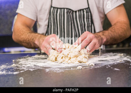 Mann Vorbereitung Pizza Teig auf schwarzem Granit Tisch Stockfoto