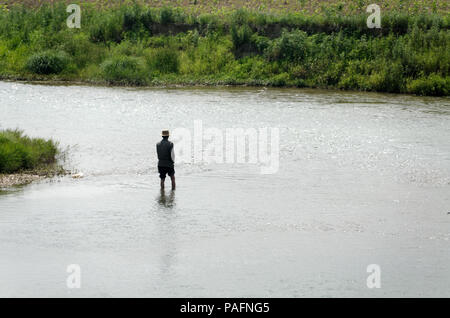 Nordkoreanische fischer Mann mit Rob in einem Fluss, der durch die Felder von Reis Stockfoto