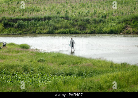 Nordkoreanische fischer Mann mit Rob in einem Fluss, der durch die Felder von Reis Stockfoto