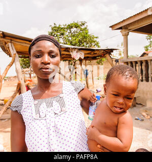 - PORTO NOVO, BENIN - Mar 8, 2012: Unbekannter beninischen Mutter trägt ihr Kind in ihren Händen Bevölkerung von Benin Leiden der Armut aufgrund der schwierigen Stockfoto