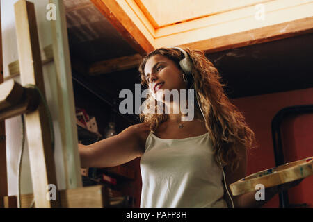 Innen- schuss von professionellen lächelnd weibliche Künstler mit Kopfhörern Gemälde auf Leinwand im Studio. Stockfoto