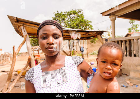 - PORTO NOVO, BENIN - Mar 8, 2012: Unbekannter beninischen Mutter trägt ihr Kind in ihren Händen Bevölkerung von Benin Leiden der Armut aufgrund der schwierigen Stockfoto