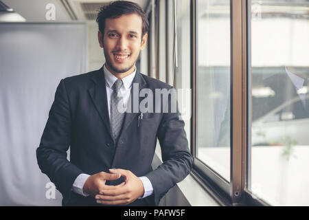 Gerne gut aussehender Geschäftsmann und lächelnd im Büro Stockfoto