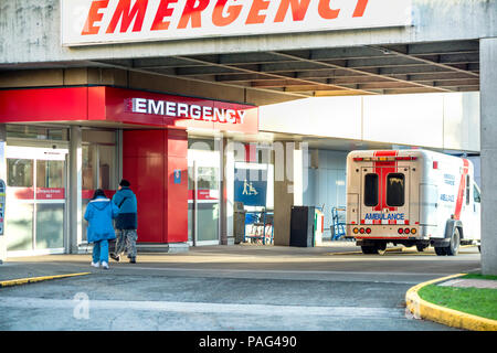Patienten gehen in das Krankenhaus zu einem Notfall Eingang, ein Notarzt und Sanitäter Auto stehen in der Nähe warten auf einen Notruf Stockfoto