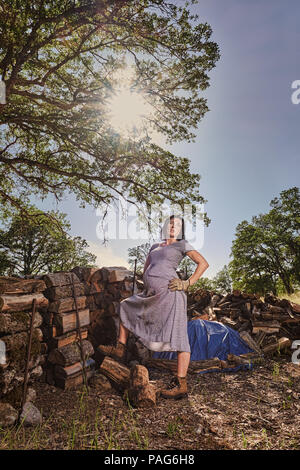 Eine schwangere Frau in einem Kleid und Schuhe Ausruhen nach dem Stapeln Holz auf einem Haufen. Stockfoto