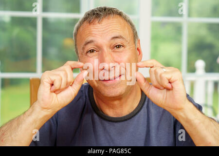 Kaukasische Mann, Allein, sitzen an einem Tisch, Tag, schauen uns an, mit einem sehr kleinen Messgeräten mit seinen Fingern. Stockfoto