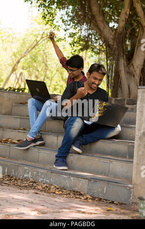 Glückliche junge Studenten arbeiten am Laptop im Park Stockfoto