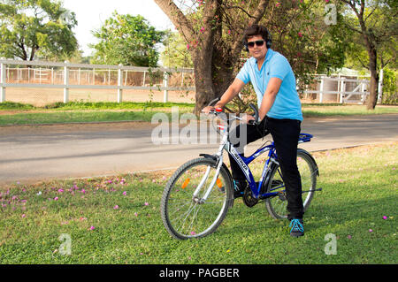 Junger Mann mit Brille Reiten Fahrrad- und Hören von Musik Stockfoto