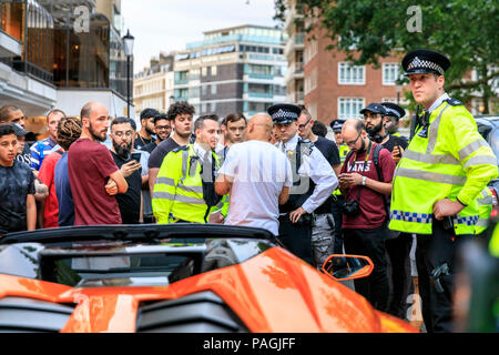 Sloane Street, London, UK, 20. Juli 2018. Polizei stoppt, dann stören Sie sich an den Eigentümer der orange Lamborghini sprechen, während eine Masse wächst rund um das Auto. Supercars, hohe Leistung und klassische Autos, sowie einige charakteristische Anpassungen, und fahren Sie entlang der Sloane Street für Supercar Sonntag, die sieht rund 400 Autos teilnehmen. Stockfoto