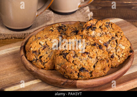 Stapel von Haferflocken pecan Rosinen Cookies auf einer rustikalen Holzmöbeln Platte mit Kaffeetassen im Hintergrund Stockfoto