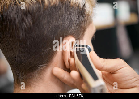 Barbier hand mit Haarschneider, neuer Haarschnitt für Client vor dem Spiegel zu sitzen. Modell in dunklen, getönten Haare, freuen. Arbeiten in modernen spacigen Friseur, Beauty Salon. Stockfoto