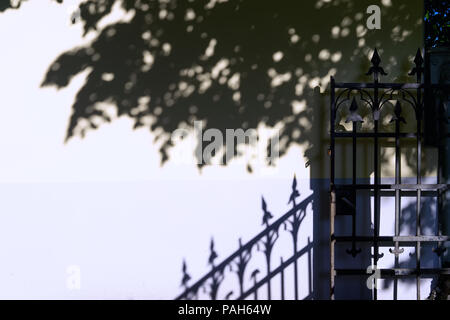 Die Schatten der Bäume und openwork Eisen Zaun an der Wand Stockfoto