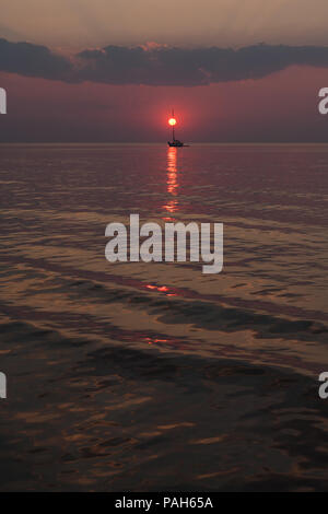 Die Sonne untergeht in den Wellen des Meeres vor dem Hintergrund der Yachten und Wolken am Horizont Stockfoto