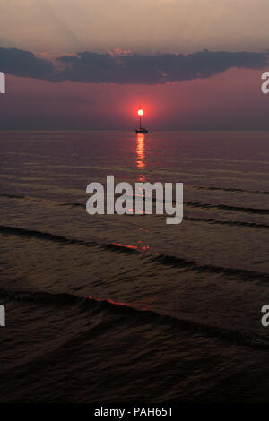 Die Sonne untergeht in den Wellen des Meeres vor dem Hintergrund der Yachten und Wolken am Horizont Stockfoto
