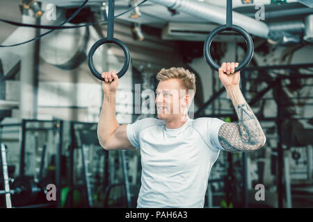 Hübscher junger Mann mit starken Armen hängend an Gymnastik Ringe Stockfoto