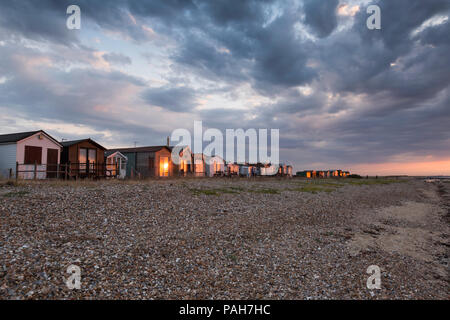 Golden Sunset Licht am Strand Hütten vom Kiesstrand an Seasalter, Whitstable, Kent, Großbritannien. Dramatische Wolken sind oben gesehen. Stockfoto